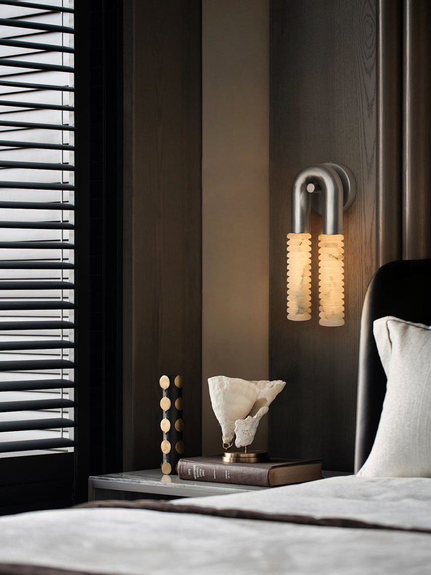 The sconce glowing in a dark bedroom above a low table with a sculpture