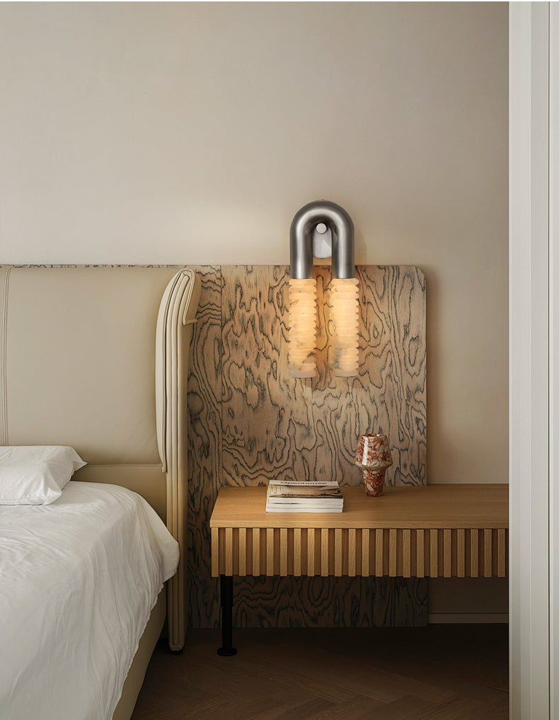 The sconce lit beside a headboard above a slatted wood nightstand