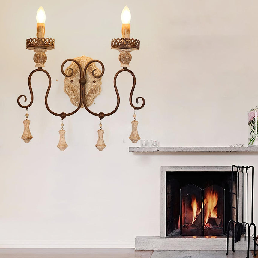 Sconce lit on a wall above a fireplace mantel with flowers and a lit fire