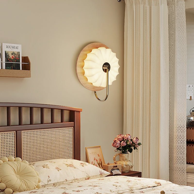 Sconce lit above a cane headboard beside a shelf of photographs and flowers