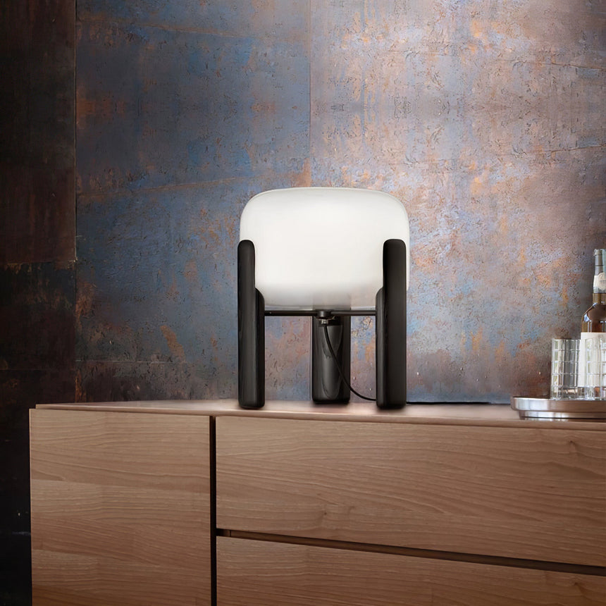 Frosted glass table lamp lit on a wood dresser against a patina wall