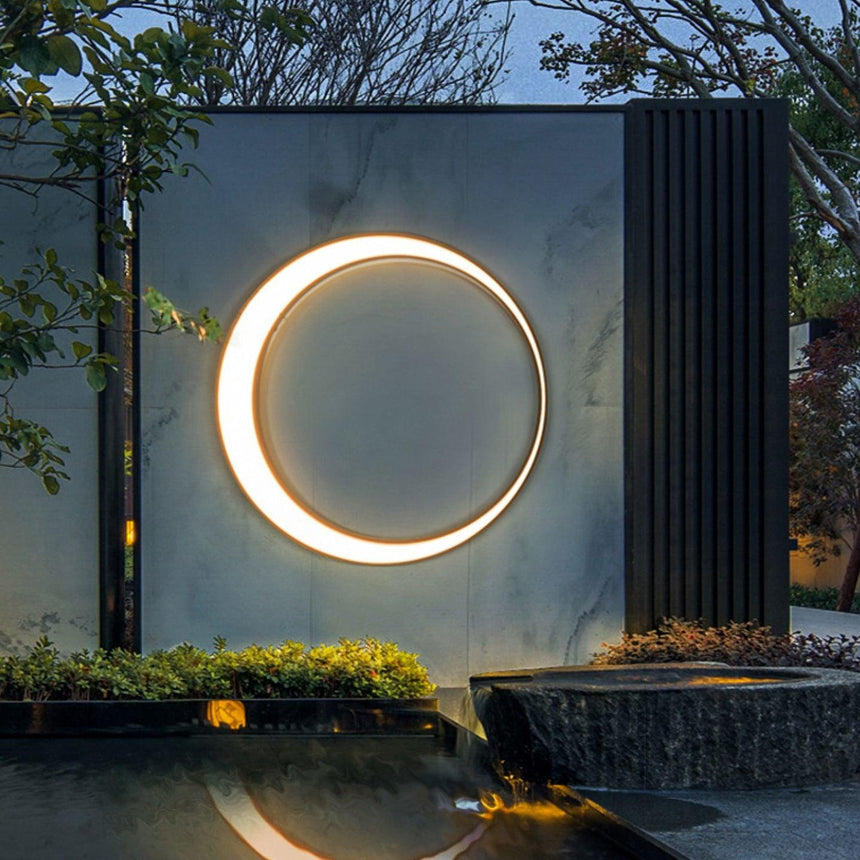 The ring lit on a stone wall above a still pool and a planted edge at dusk