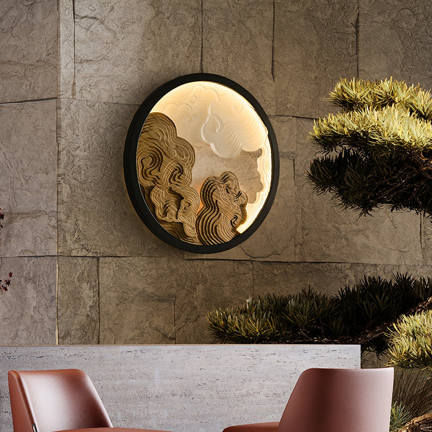 Sconce lit on a stone wall above two chairs with a clipped plant beside