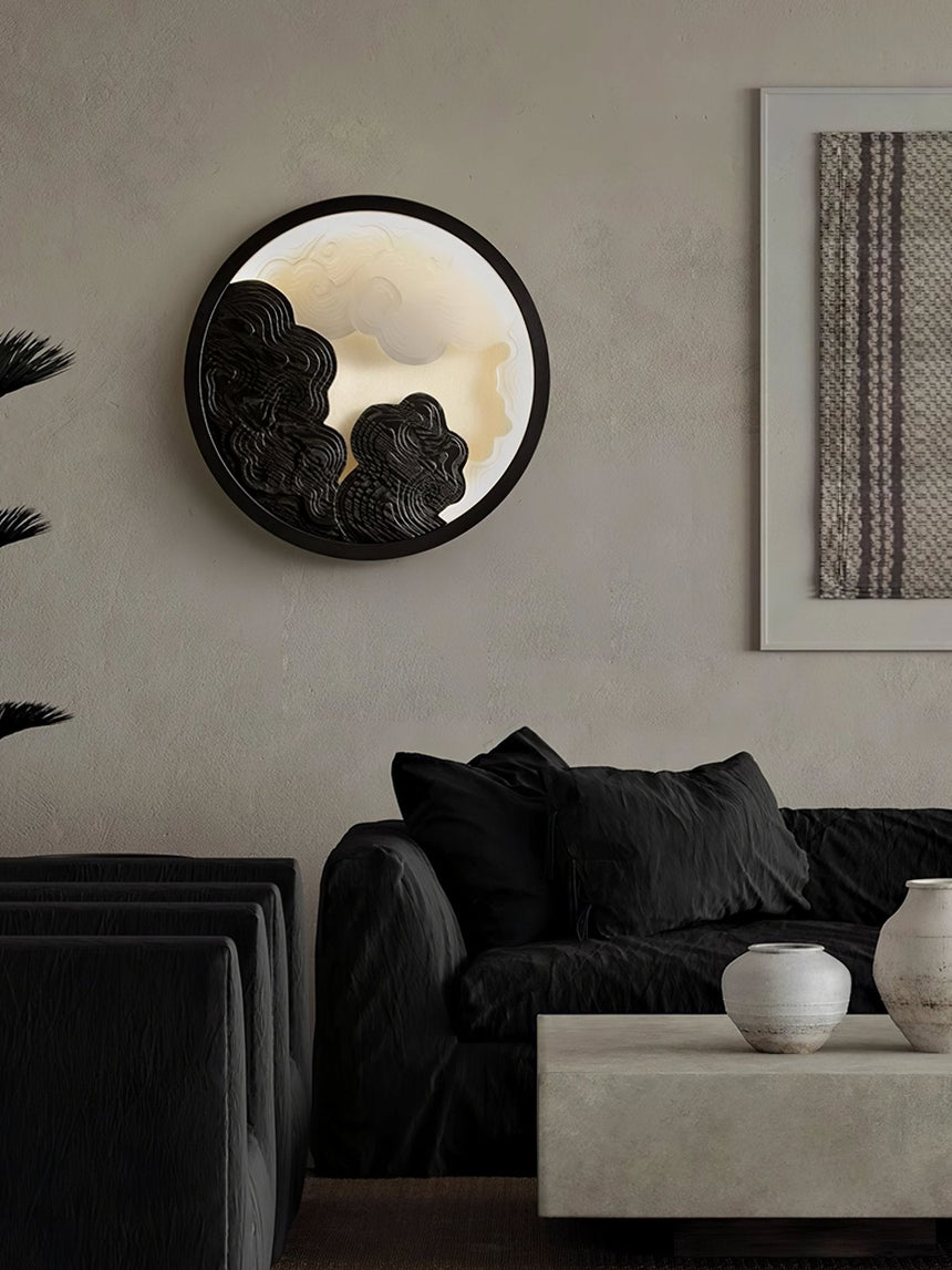 Sconce lit beside a framed textile above a dark sofa with cushions