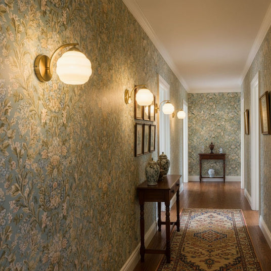 A row of gold sconces lit along a hallway with patterned wallpaper and a runner