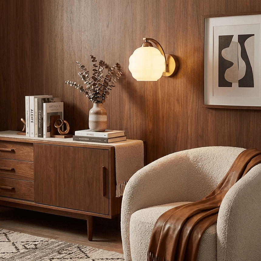 The gold sconce lit on a wood paneled wall above a sideboard and an armchair