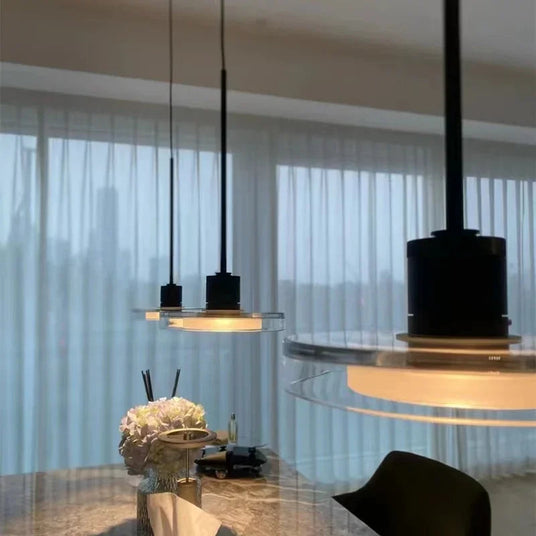 Two disc pendants above a dining table in front of a sheer curtained window