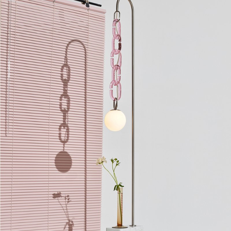 The pink glass chain and lit globe beside a pink window blind, a vase of flowers below