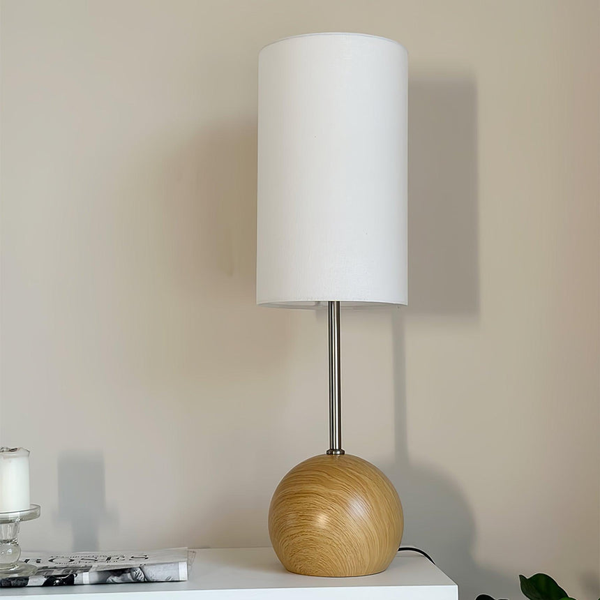 Natural wood globe table lamp lit on a white console beside a plant