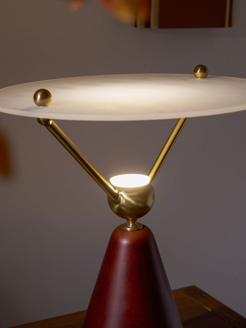 Gold and white table lamp lit on a chest behind a blossom branch