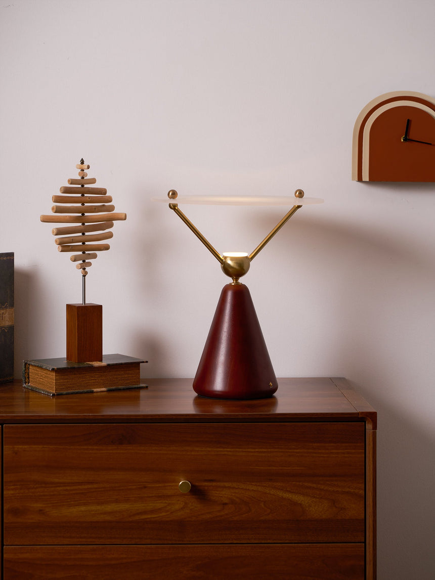 Gold and white table lamp on a walnut dresser beside a brass object