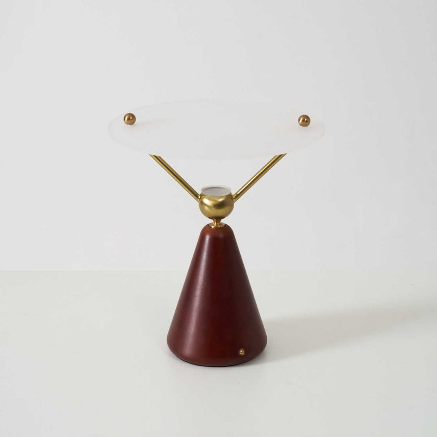 Gold and white table lamp seen from the front against a plain ground