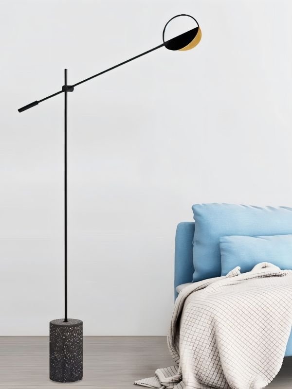 The lit lamp reaching over a bed with blue bedding beside a white wall