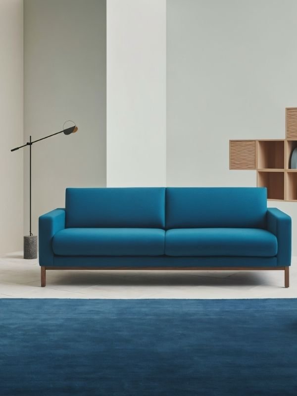 The lit lamp reaching over a blue sofa with cushions on a deep blue rug