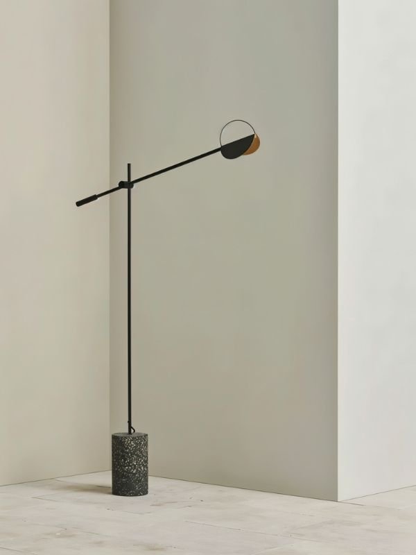 The shallow disc shade at the end of the arm, tipped down toward the floor below