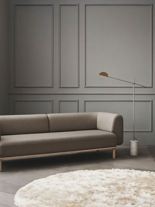 The lit lamp reaching over a long sofa against a gray paneled wall with a rug