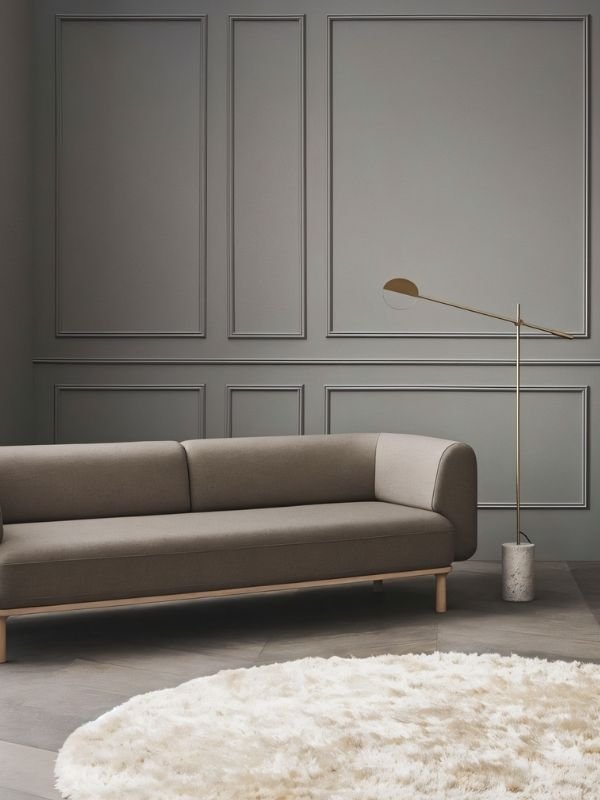 The lit lamp reaching over a long sofa against a gray paneled wall with a rug