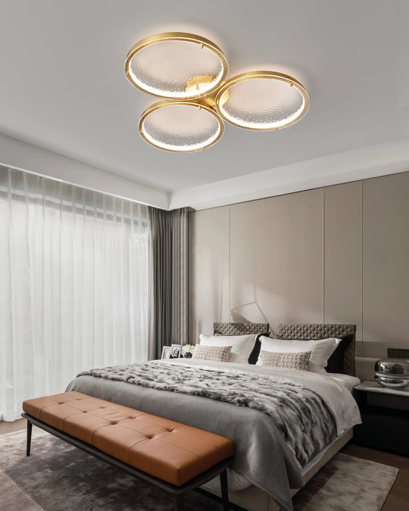 Three ring gold ceiling light above a bed and a leather bench