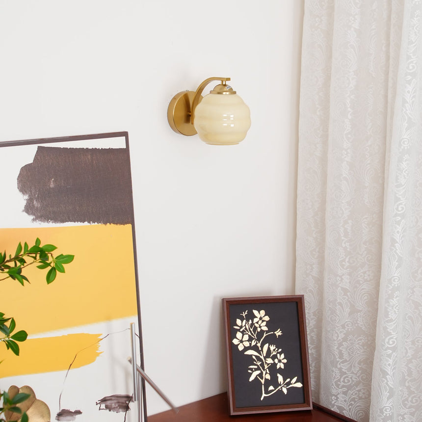 The gold sconce lit above a leaning abstract canvas and a small framed print