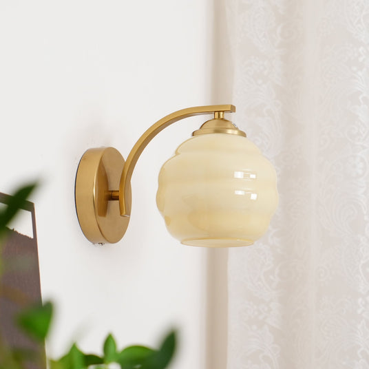 The gold sconce with a beige globe beside a lace curtain and a green plant