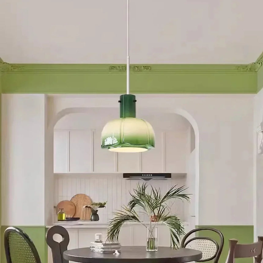 The green glass shade lit above a round table against a green painted wall
