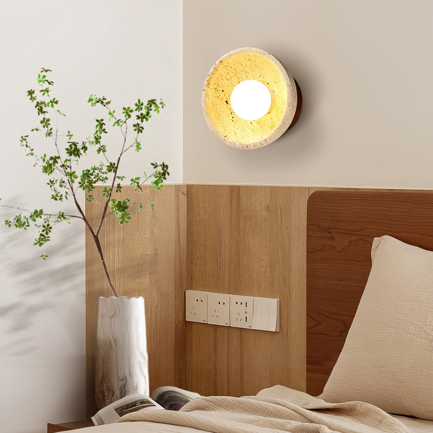 Sconce lit above a bed with a wood headboard and a vase of branches