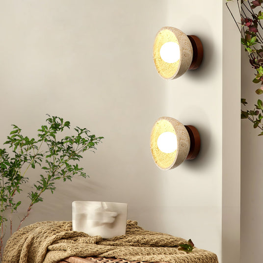 Two sconces lit above a bench with a knit throw and a branch in a vase