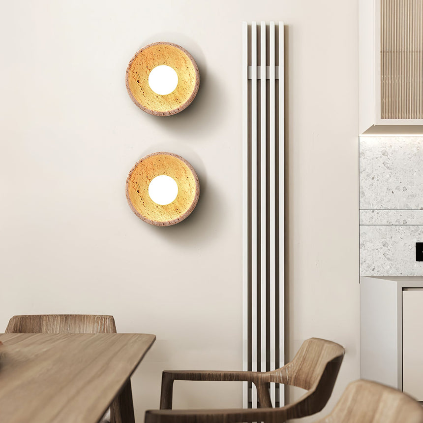 Two sconces lit on a dining wall above a wood table and curved chairs