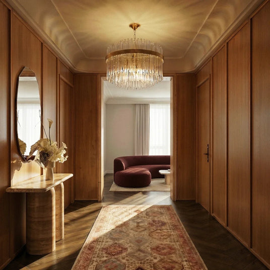 The lit fitting in a hallway above a runner rug, a console table and a round mirror