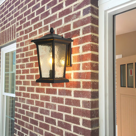 The lantern lit on red brick beside a white front door and a window