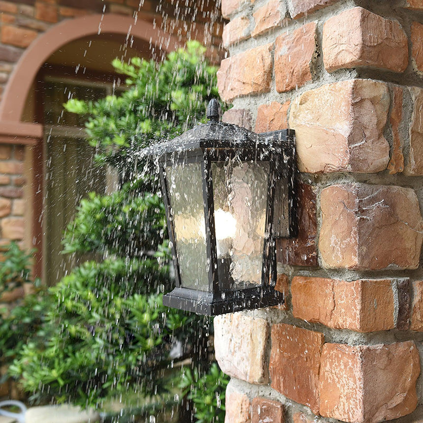 The lantern lit in heavy rain on a stone wall beside a climbing plant