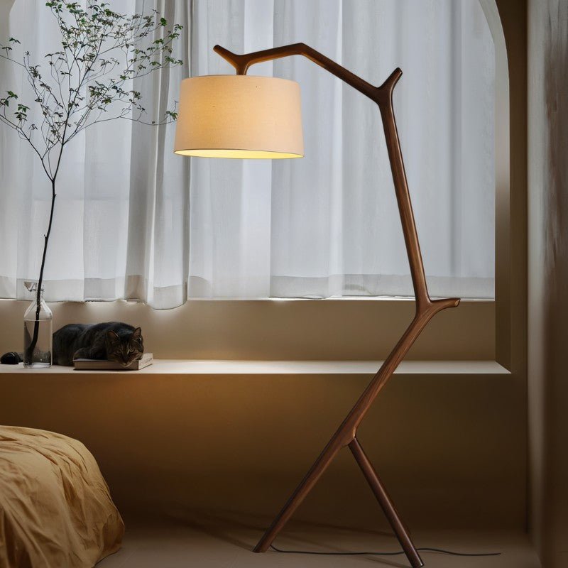 The lit lamp beside a bed and a window seat with sheer curtains and a plant