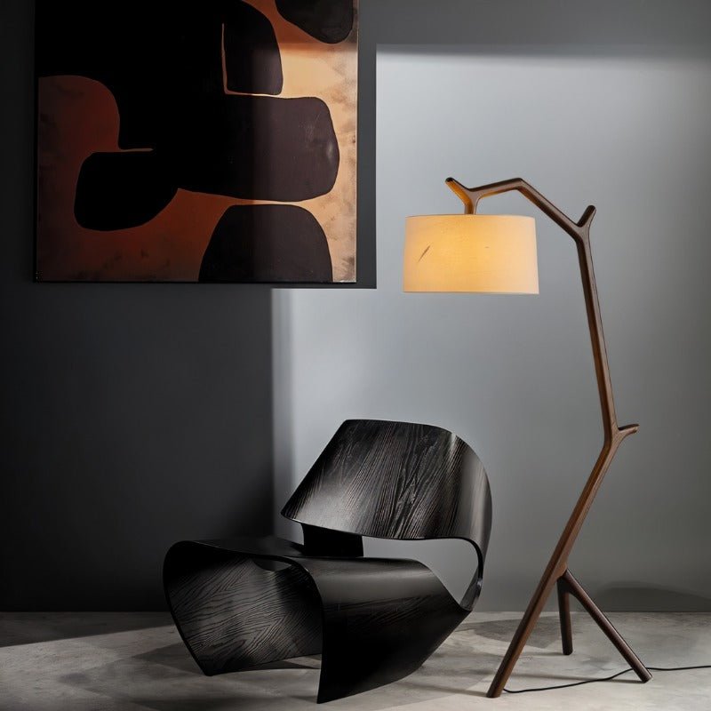 The lit lamp beside a black molded chair with abstract artwork on the wall behind