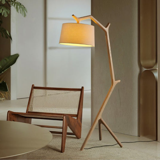 The lit lamp leaning over a cane and timber lounge chair on a pale stone floor