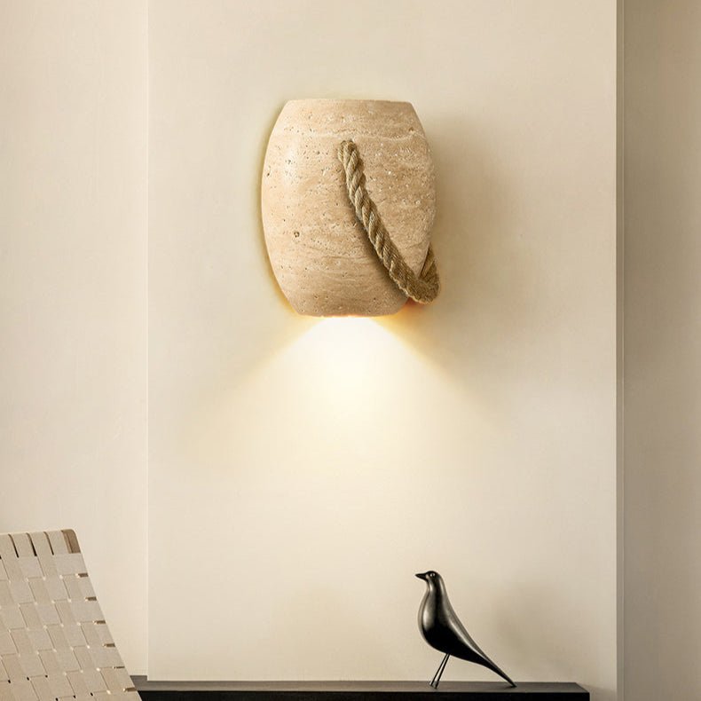 The travertine urn lit above a black floating shelf with a bird figure, a woven chair below