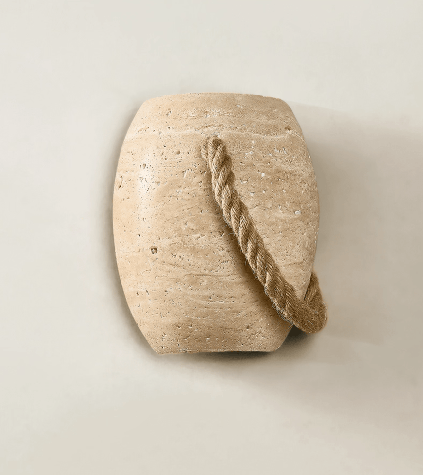 The urn unlit on a cream wall, the travertine pores and the rope loop clear