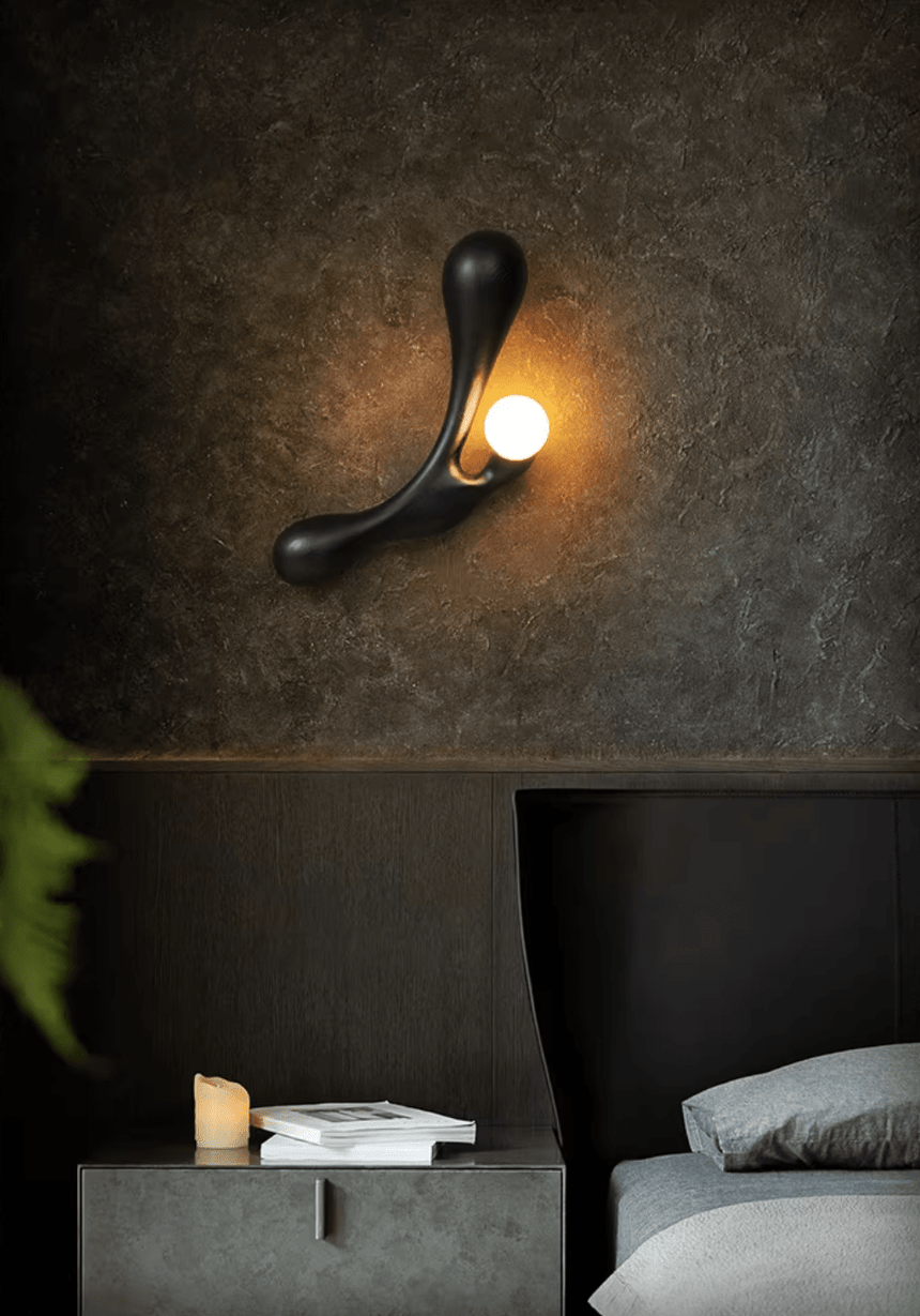 Sconce lit above a low bed beside a tray of ceramics on a dark surface