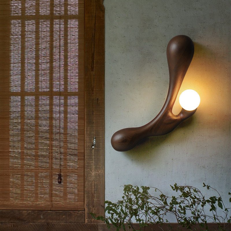 Sconce lit on a courtyard wall beside a wood screen and green leaves
