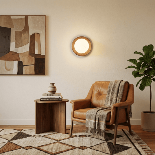 Sconce lit above a round wood table beside an armchair and a tall plant