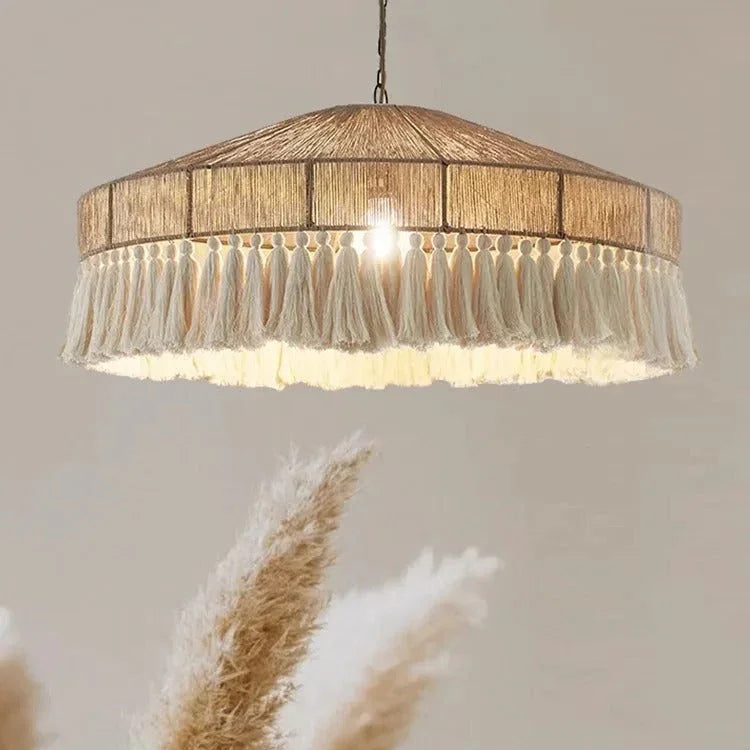 Jute pendant light with a fringed drum shade lit above dried grasses