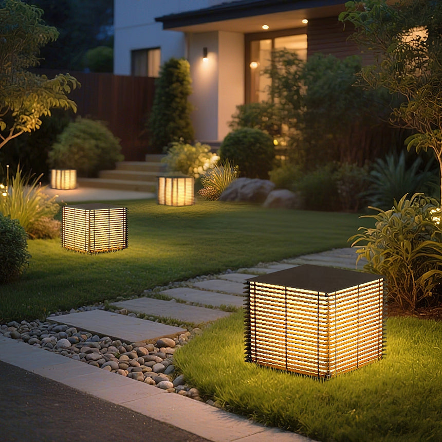 The cube glowing on a lawn with shrubs and a path behind it at night