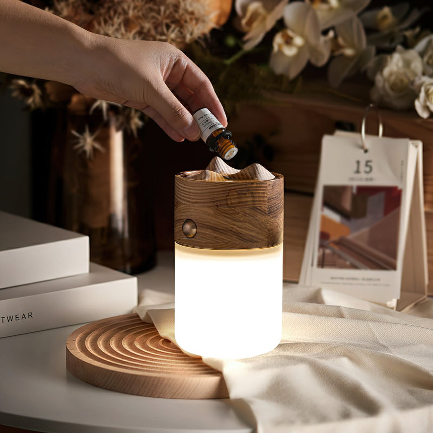 A hand dripping essential oil onto the carved ash top of the lit lantern