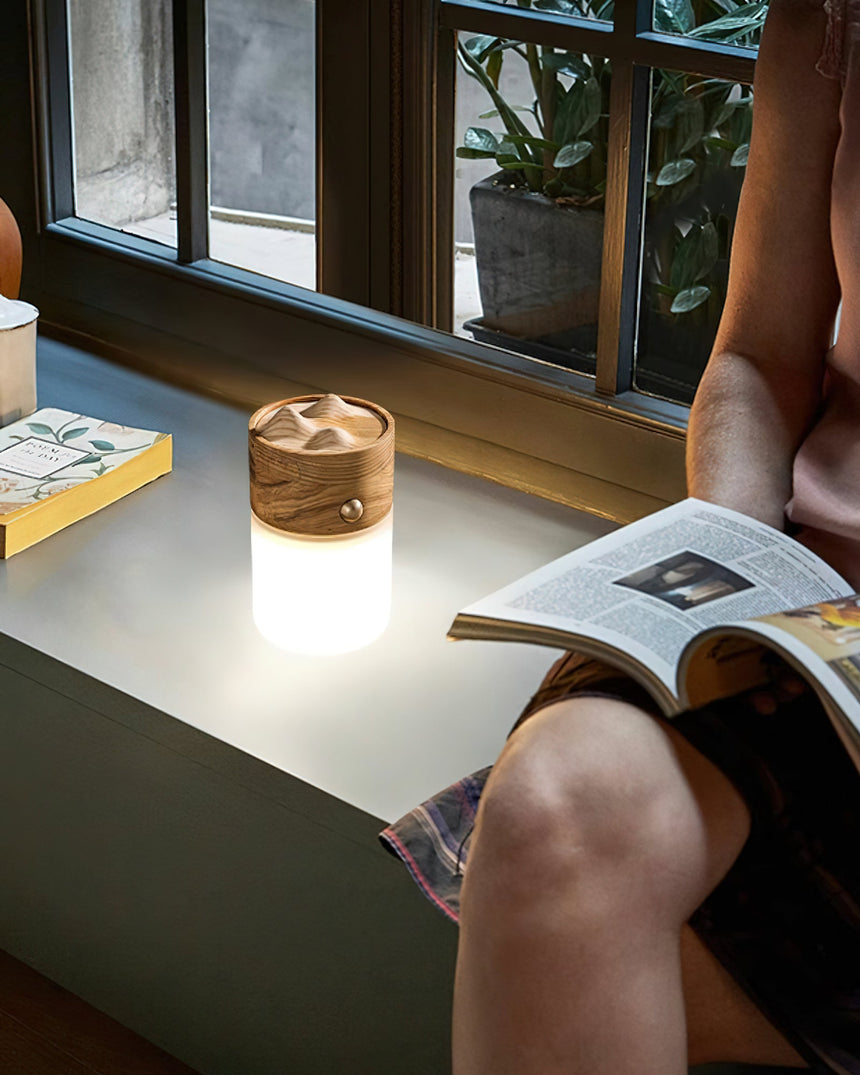 Lantern table lamp lit on a window seat beside someone reading