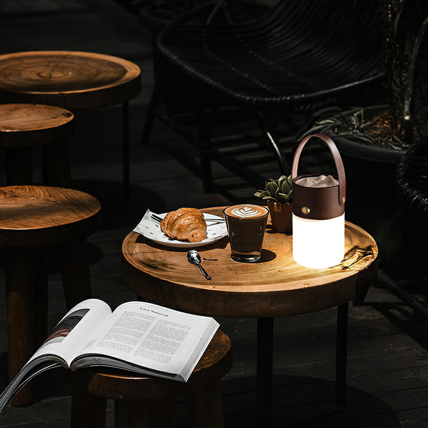 Lantern table lamp lit on a round table beside a book and a pastry