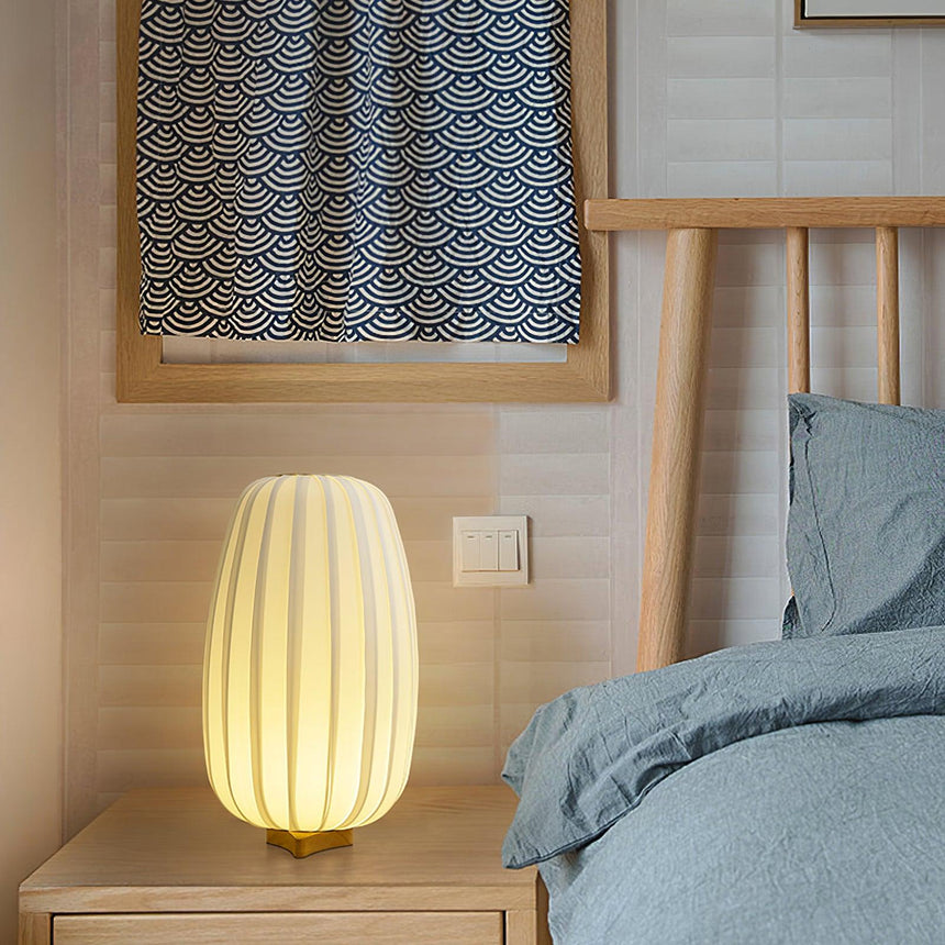 Pleated lantern lamp lit on a bedside table against a wood headboard