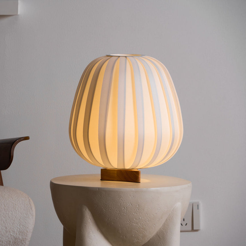 Pleated lantern lamp lit on a pale plinth beside an armchair