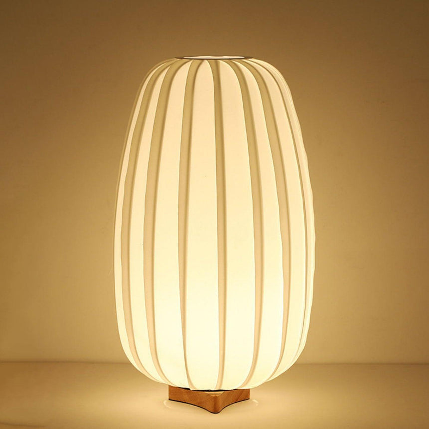 Tall pleated lantern lamp lit warm, the ribs glowing from inside