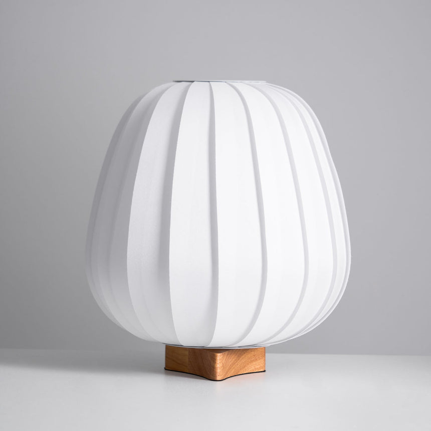 Tall pleated fabric lantern lamp unlit on a small wood cross foot