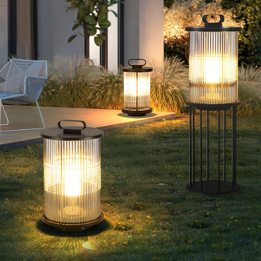Two lanterns lit on a lawn at dusk with grasses and a house behind them
