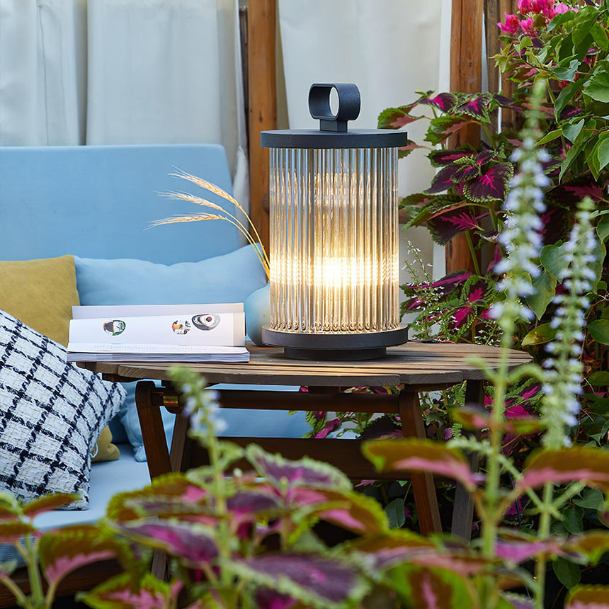 The lantern lit on a low table with planting and a cushion behind it